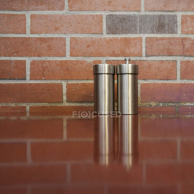 Salt e pimentão shakers na mesa com parede de tijolo atrás. — Fotografia de Stock