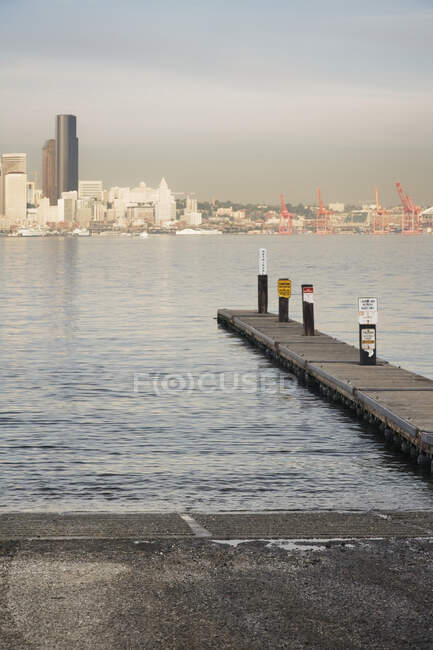 Muelle en el agua en el paseo marítimo urbano con rascacielos más allá. - foto de stock