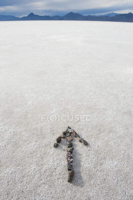 Pebbles arranged on salt flat in the shape of an arrow. — Stock Photo