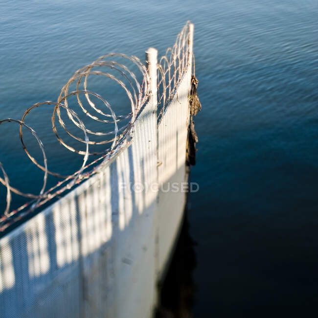 Valla de hierro corrugado y alambre de púas en el océano - foto de stock
