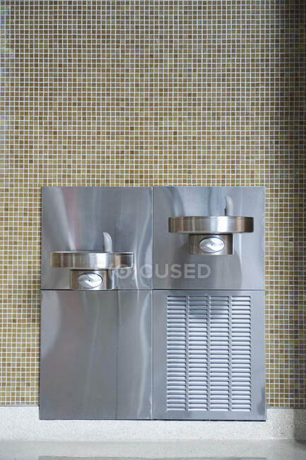 Trinkbrunnen aus Metall an Mosaik-Fliesenwand. — Stockfoto