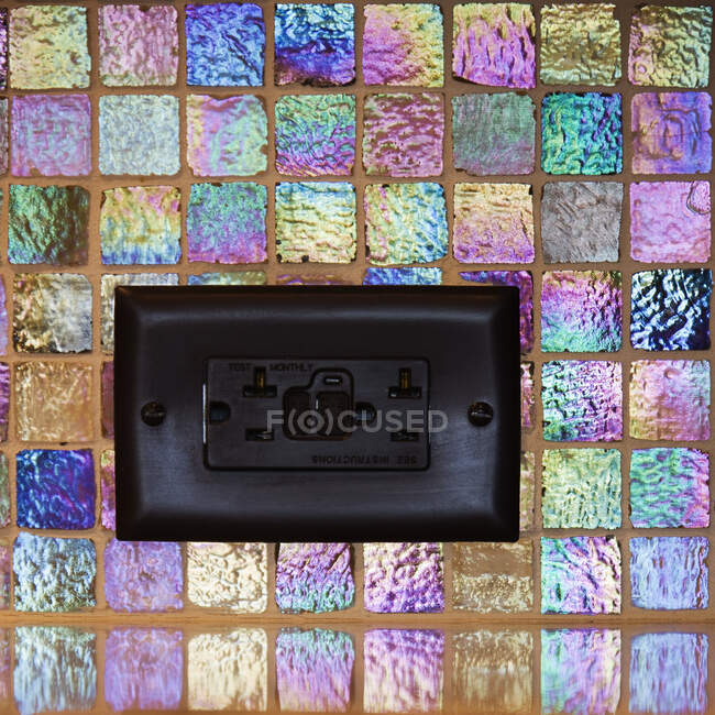 Enchufe negro en azulejo de mosaico de colores. - foto de stock