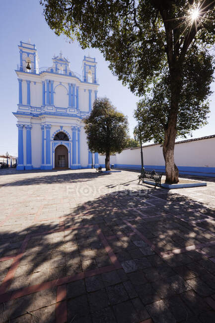 Church in a town square and a shady bench under a tree — Stock Photo
