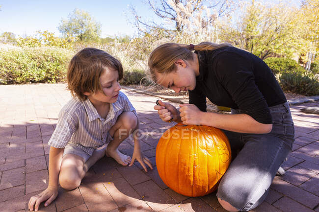 Adolescente y su hermano menor tallando calabazas en el patio. - foto de stock