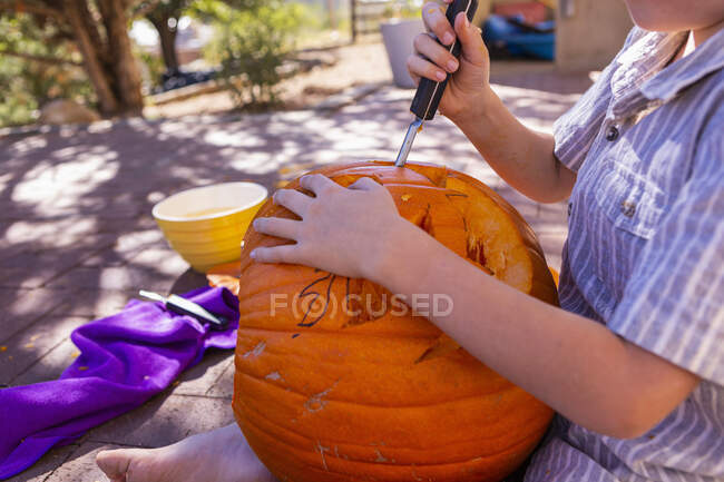 Young boy carving pumpkin on patio. — Stock Photo