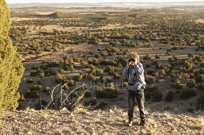 Jovem rapaz em Galisteo Basin olhando através de binóculos ao pôr do sol — Fotografia de Stock
