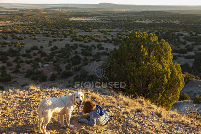 Young boy in Galisteo Basin at sunset with his English Cream Golden Retreiver — Stock Photo