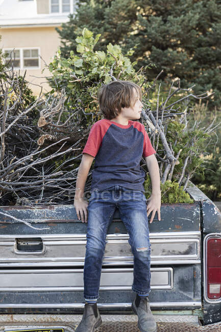 Jeune garçon assis sur une vieille camionnette pleine de broussailles — Photo de stock