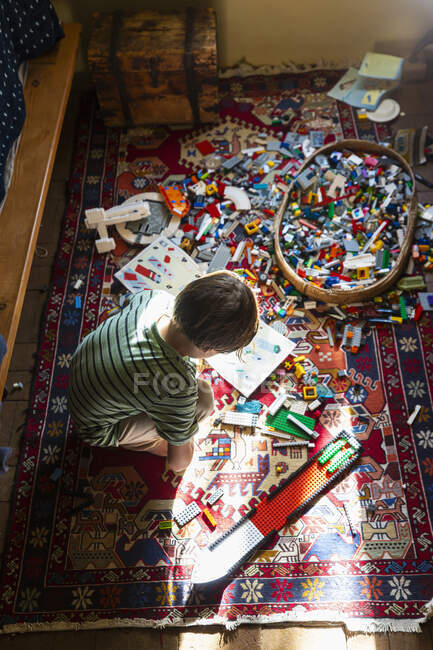 Хлопчик сидить серед іграшок на підлозі своєї спальні на плямі сонячного світла — стокове фото