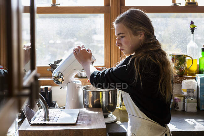 Девочка-подросток на кухне по рецепту выпечки на ноутбуке. — стоковое фото