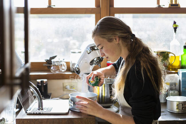 Adolescente em uma cozinha após uma receita de cozimento em um laptop. — Fotografia de Stock