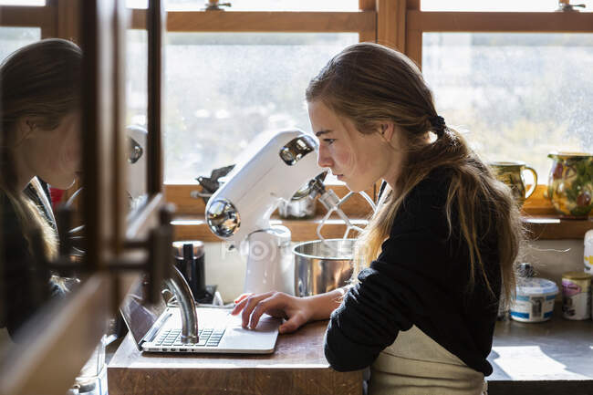 Дівчина-підліток на кухні після рецепту випічки на ноутбуці . — стокове фото