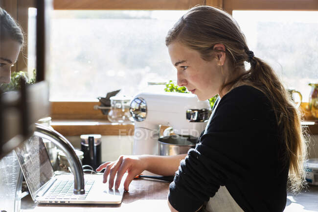 Adolescente em uma cozinha após uma receita de cozimento em um laptop. — Fotografia de Stock