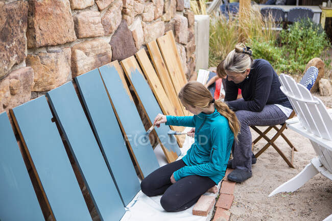 Девочка-подросток и ее мать красили деревянные полки в синий цвет на террасе — стоковое фото