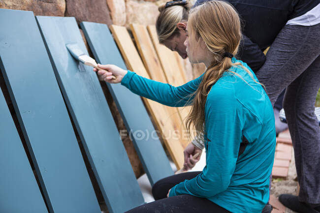 Teenagermädchen und ihre Mutter streichen Holzregale auf einer Terrasse blau an — Stockfoto