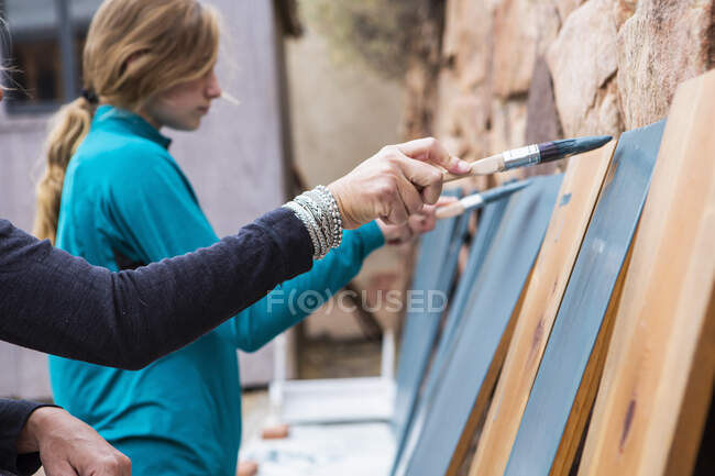 Adolescente menina e sua mãe pintando prateleiras de madeira azul em um terraço — Fotografia de Stock