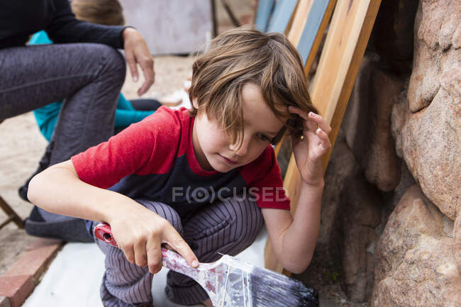 Seven year old boy using a paintbrush, painting cardboard — Stock Photo