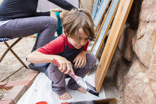 Seven year old boy using a paintbrush, painting cardboard — Stock Photo