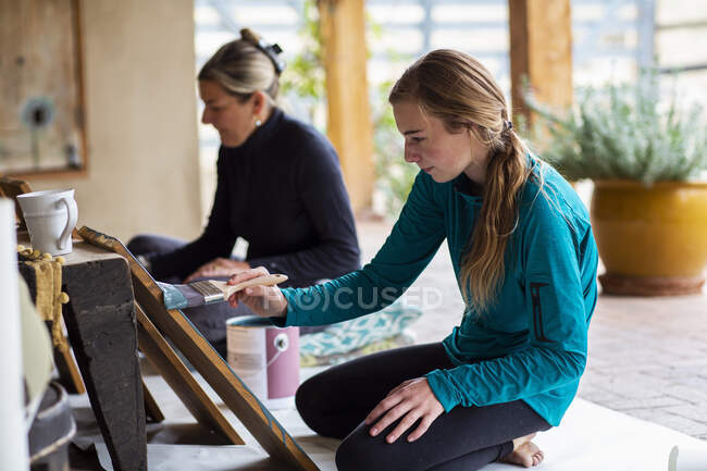 Adolescente menina e sua mãe pintando prateleiras de madeira azul em um terraço — Fotografia de Stock