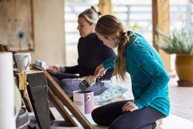Teenagermädchen und ihre Mutter streichen Holzregale auf einer Terrasse blau an — Stockfoto