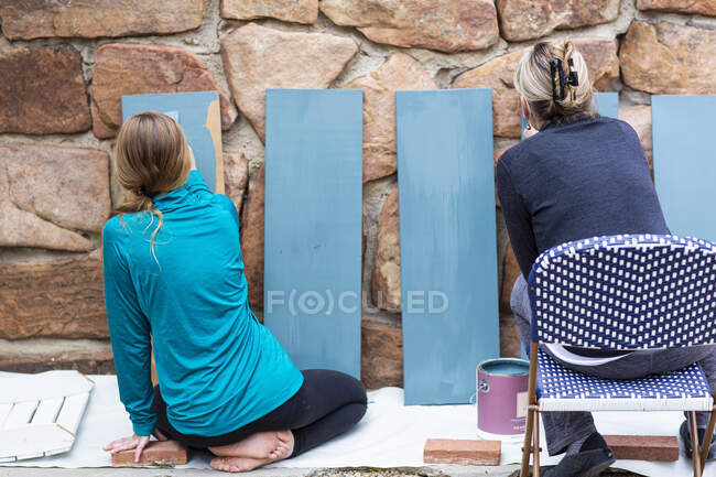 Adolescente y su madre pintando estantes de madera azul en una terraza - foto de stock