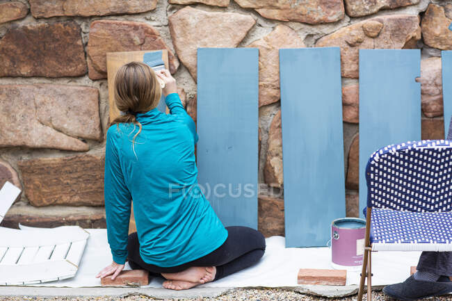 Teenage girl painting wooden shelves blue. — Stock Photo