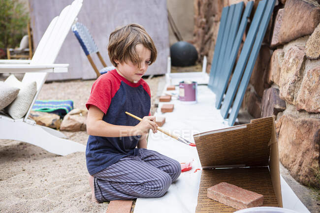 Семирічний хлопчик використовує пензлик, картон — стокове фото