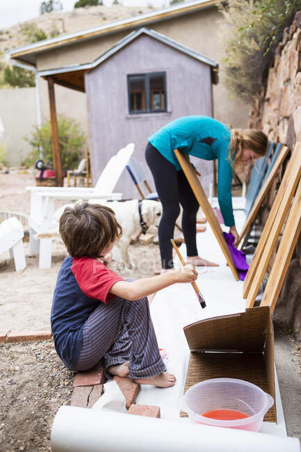 Adolescente y un niño de siete años pintando estantes con pintura azul. - foto de stock
