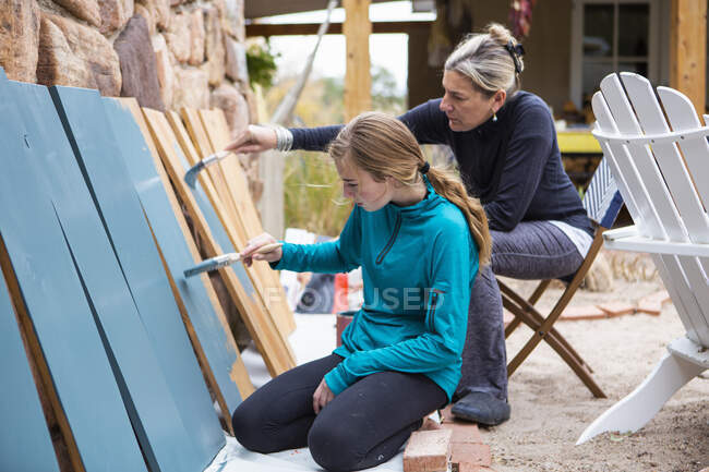 Дівчинка-підліток і її мати малюють дерев'яні полиці синіми на терасі — стокове фото