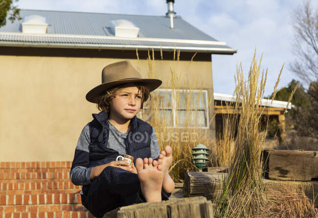 Портрет мальчика в шляпе-шляпе, расслабляющего на крыльце — стоковое фото
