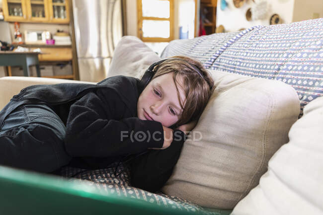 Jovem deitado no sofá olhando para o computador portátil — Fotografia de Stock