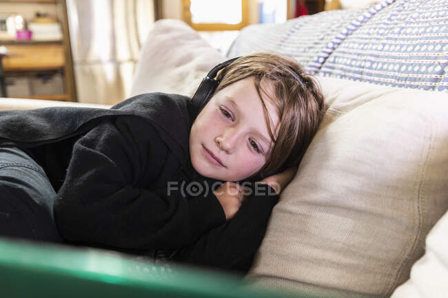 Young boy lying on sofa looking at laptop computer — Stock Photo