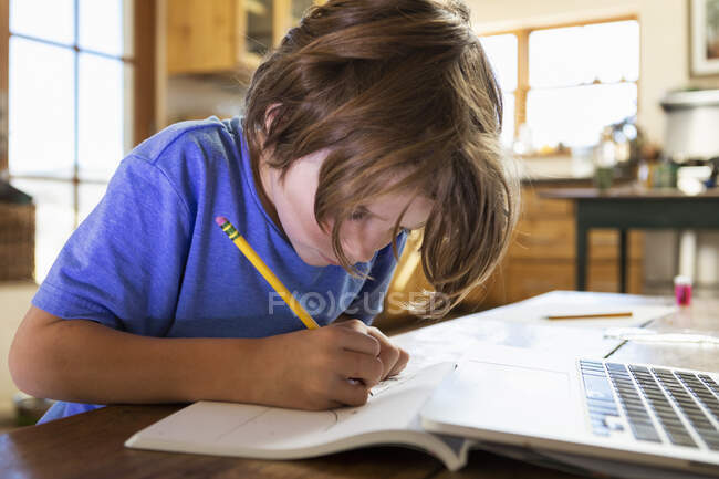Niño en casa escribiendo y dibujando en su bloc de dibujo - foto de stock