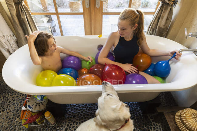 Joven niño y su hermana mayor en la bañera llena de globos de agua - foto de stock