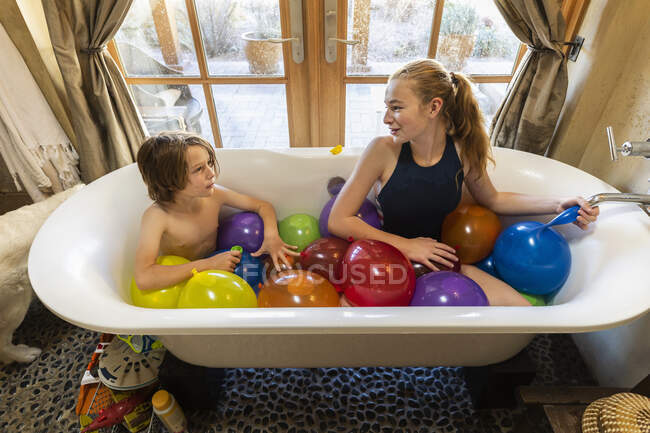 Young boy and his older sister in bathtub filled with water balloons — Stock Photo