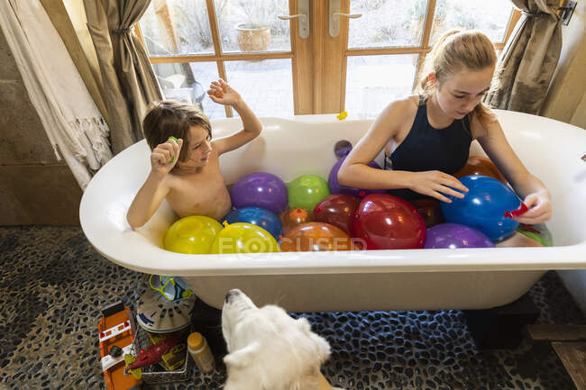 Jovem e sua irmã mais velha na banheira cheia de balões de água — Fotografia de Stock