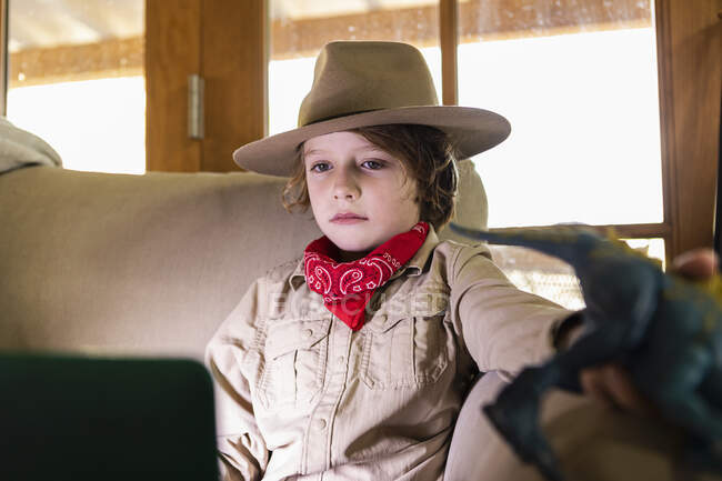 Menino vestindo roupa de safári e fones de ouvido assistindo a um filme no laptop — Fotografia de Stock