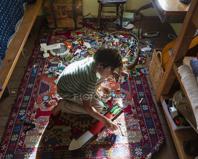 Мальчик сидит среди игрушек на полу своей спальни в лучах солнечного света — стоковое фото