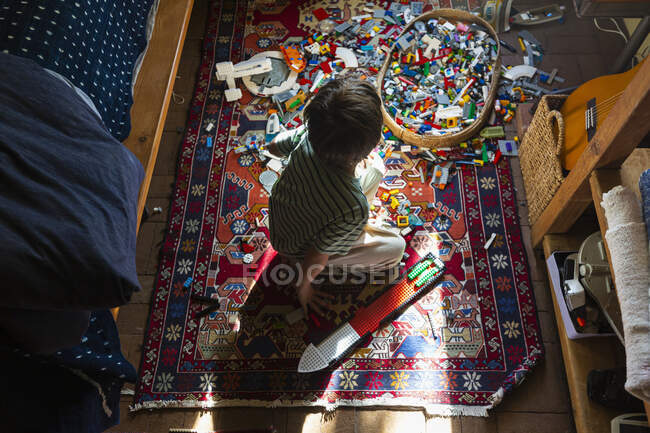 Menino sentado entre brinquedos no chão de seu quarto em um pedaço de luz solar — Fotografia de Stock