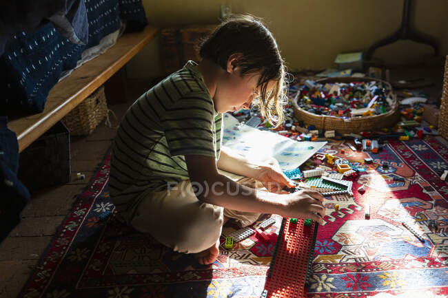 Niño sentado entre juguetes en el suelo de su dormitorio en un parche de luz solar - foto de stock