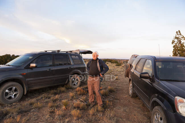 Senior man between SUV cars at sunset, Galisteo Basin, Santa Fe, NM — Fotografia de Stock