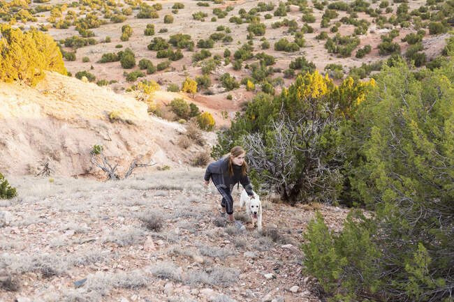 Adolescente grimpant une pente suivant son chien golden retriever — Photo de stock