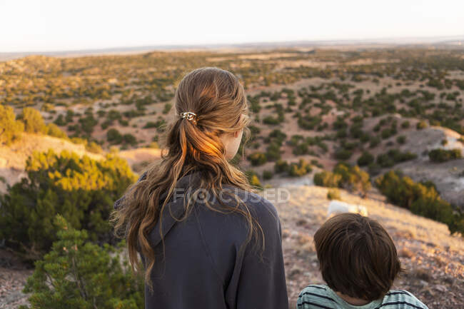 Teenage girl and her brother looking down at Galisteo Basin, Santa Fe, at sunset — Stock Photo