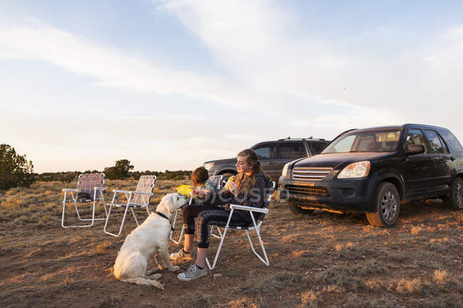 Crianças sentadas em cadeiras de gramado jantando, um cão ao lado deles — Fotografia de Stock