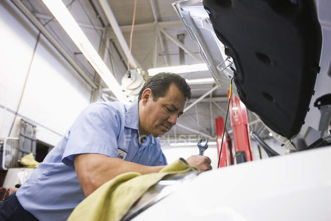 Hispanic mechanic leaning into an engine of a car he working on in an auto repair shop — Stock Photo