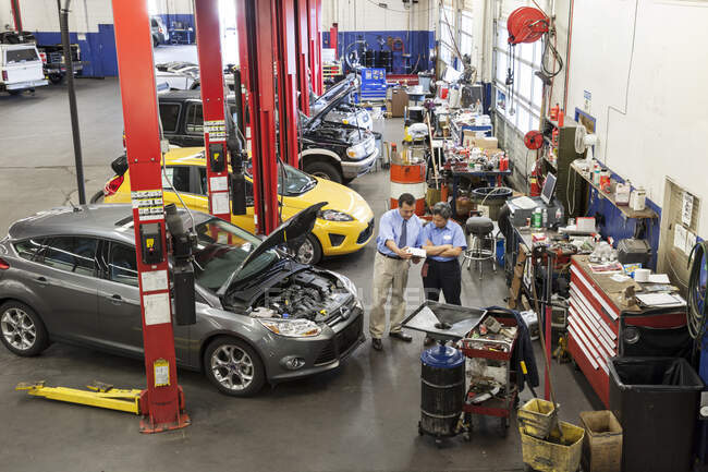 Propriétaire d'un atelier de réparation automobile parlant avec la mécanicienne hispanique — Photo de stock