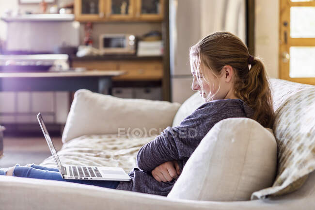 Девочка-подросток смотрит на ноутбук на диване — стоковое фото