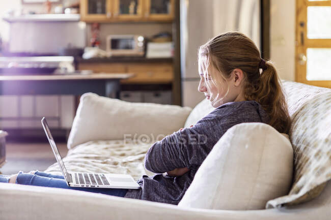Teenagermädchen schaut auf Laptop auf Sofa — Stockfoto
