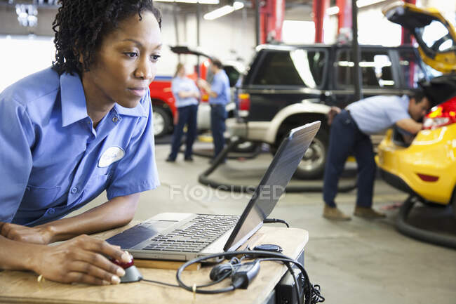 Meccanica femminile che utilizza un computer portatile, elettronica diagnostica, in un'officina di riparazione auto — Foto stock