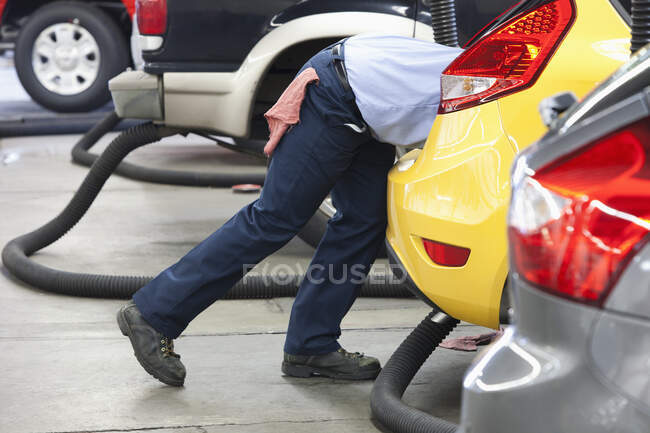 Mecânico de automóveis em uma oficina de reparação, inclinando-se para um carro, trabalhando nele. — Fotografia de Stock
